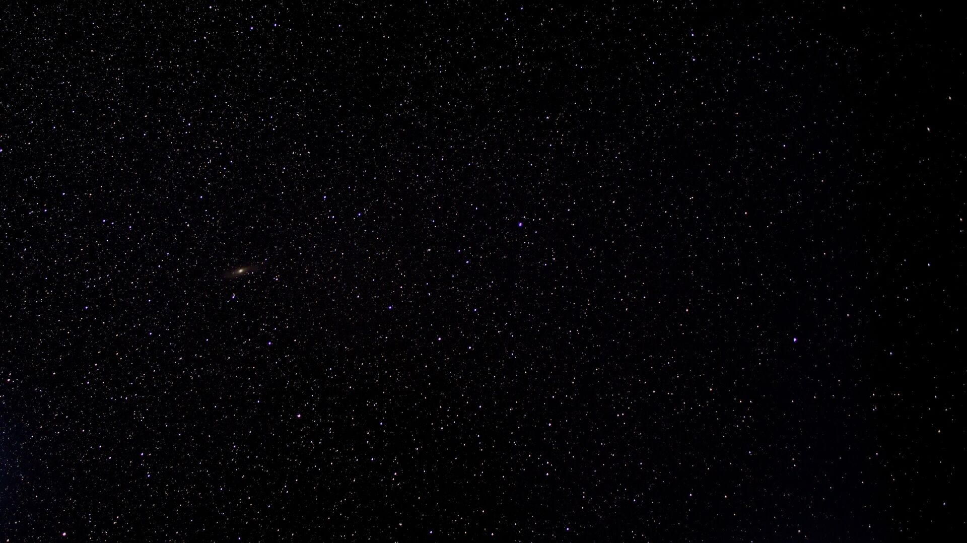 Final edited astrophotography image of a starry night sky including the Andromeda galaxy on the left and stars trailing off to black on the right.